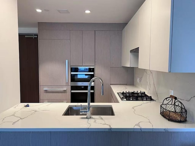 kitchen with gas cooktop, gray cabinets, modern cabinets, a sink, and light stone counters