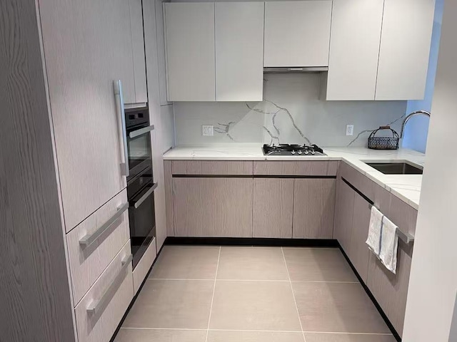 kitchen featuring stainless steel gas cooktop, light stone countertops, under cabinet range hood, a sink, and light tile patterned floors