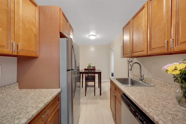 kitchen featuring light wood finished floors, brown cabinets, a sink, light countertops, and appliances with stainless steel finishes