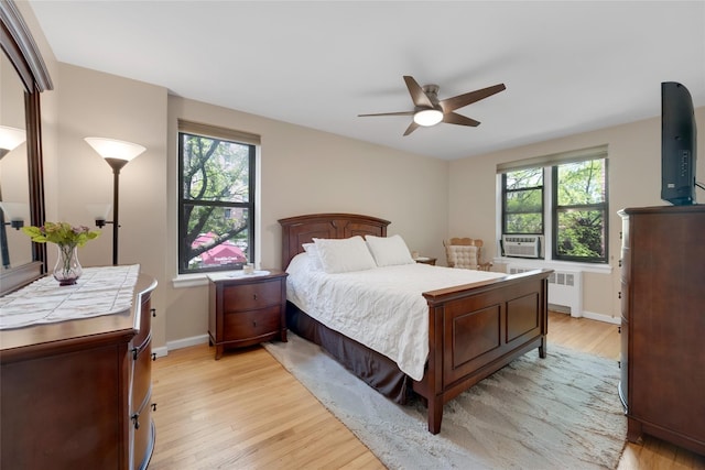 bedroom featuring a ceiling fan, baseboards, radiator, cooling unit, and light wood finished floors