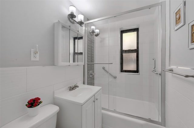 bathroom featuring tile walls, toilet, vanity, and combined bath / shower with glass door