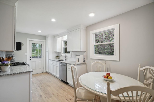kitchen with a sink, dishwasher, light wood finished floors, backsplash, and white cabinets