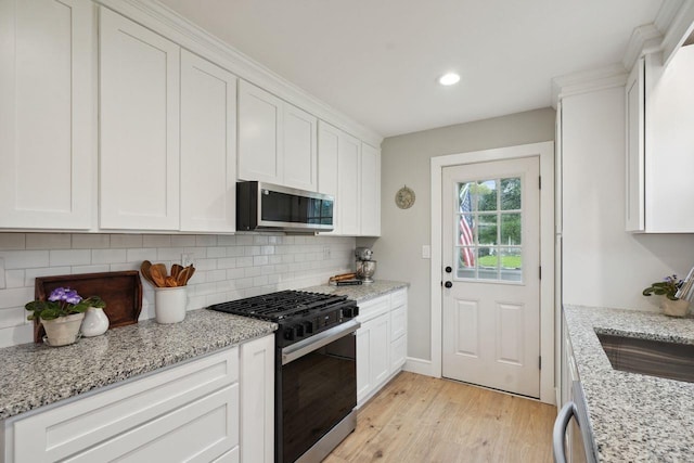 kitchen with stainless steel microwave, a sink, light wood finished floors, white cabinetry, and range with gas cooktop