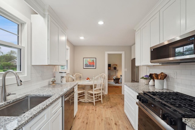 kitchen with a sink, light wood-style flooring, white cabinets, and appliances with stainless steel finishes