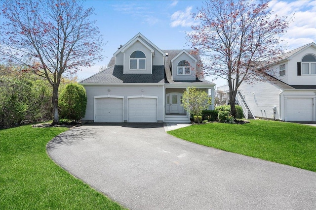 view of front of home with an attached garage, a front lawn, roof with shingles, and aphalt driveway