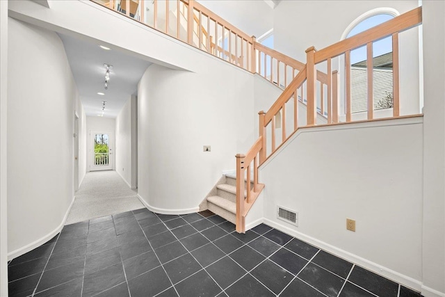 stairs with a high ceiling, tile patterned flooring, carpet, baseboards, and visible vents