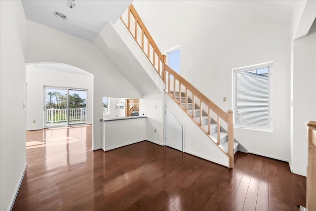 stairway with arched walkways, a high ceiling, baseboards, and hardwood / wood-style floors