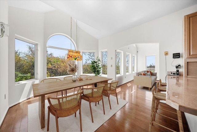 dining area featuring arched walkways, high vaulted ceiling, a wealth of natural light, and hardwood / wood-style floors