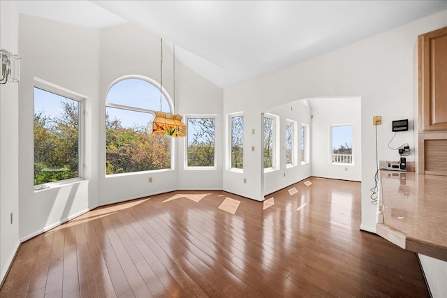 unfurnished living room featuring wood-type flooring, arched walkways, a healthy amount of sunlight, and high vaulted ceiling