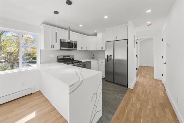 kitchen with a peninsula, light stone countertops, white cabinets, a sink, and appliances with stainless steel finishes