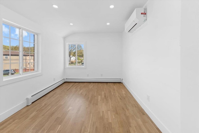 spare room featuring a baseboard heating unit, a wall unit AC, a healthy amount of sunlight, and wood finished floors