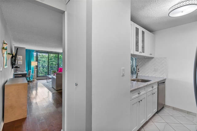 interior space featuring a sink, a textured ceiling, stainless steel dishwasher, baseboards, and tasteful backsplash