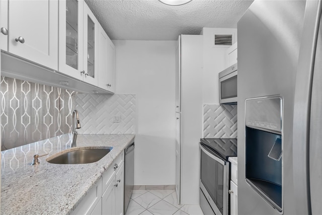 kitchen with a sink, stainless steel appliances, a textured ceiling, glass insert cabinets, and white cabinets