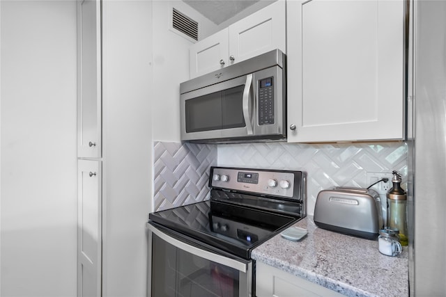 kitchen with tasteful backsplash, visible vents, white cabinets, light stone countertops, and appliances with stainless steel finishes