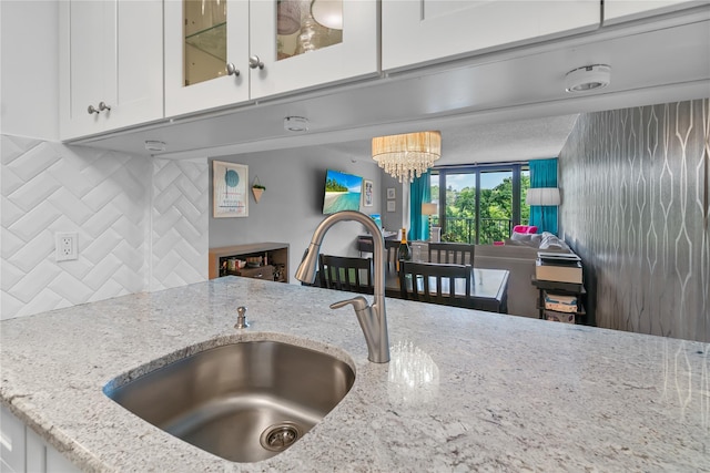 kitchen with glass insert cabinets, light stone counters, a sink, white cabinetry, and decorative backsplash