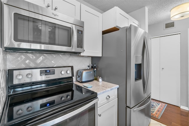 kitchen with stainless steel appliances, white cabinets, a textured ceiling, visible vents, and light countertops