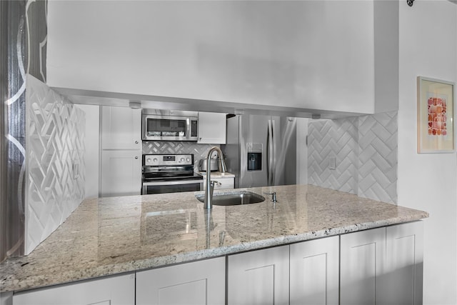 kitchen featuring a sink, tasteful backsplash, white cabinets, light stone countertops, and appliances with stainless steel finishes