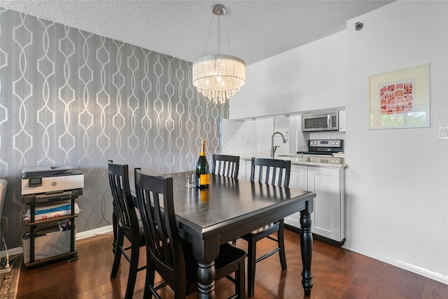 dining room featuring wallpapered walls, a notable chandelier, a textured ceiling, dark wood-type flooring, and baseboards
