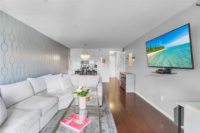 living room with dark wood finished floors, a textured ceiling, a chandelier, and baseboards