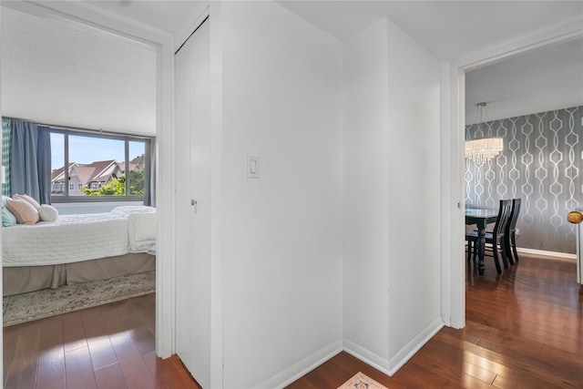 corridor with baseboards, wood-type flooring, and a notable chandelier