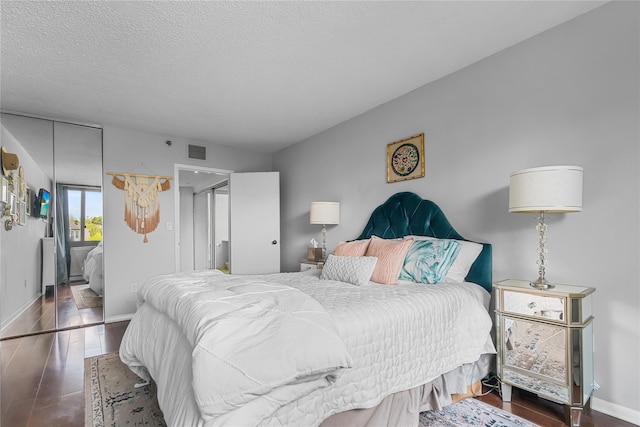 bedroom with a textured ceiling, visible vents, wood finished floors, and baseboards