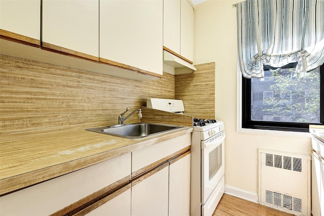 kitchen featuring radiator, white range with gas stovetop, white cabinetry, tasteful backsplash, and a sink