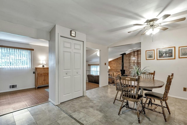 dining room featuring lofted ceiling, baseboards, ceiling fan, visible vents, and a wood stove
