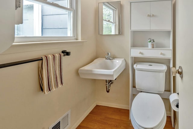 half bath featuring a sink, toilet, wood finished floors, visible vents, and baseboards
