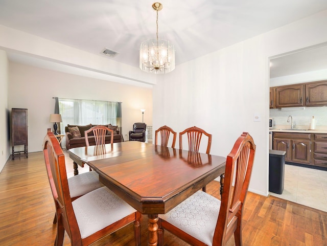 dining space featuring visible vents, light wood-style floors, and a notable chandelier
