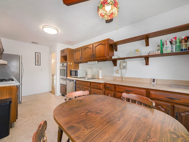 kitchen featuring brown cabinetry, appliances with stainless steel finishes, open shelves, a sink, and light countertops