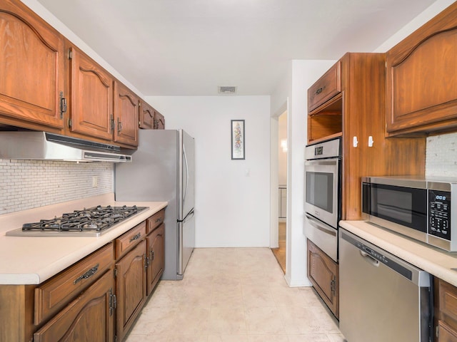 kitchen featuring appliances with stainless steel finishes, light countertops, brown cabinetry, backsplash, and a warming drawer