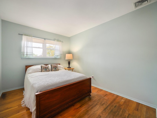 bedroom with baseboards, visible vents, and wood finished floors