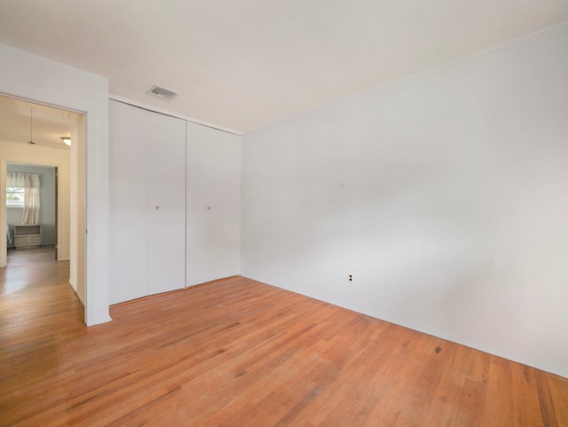 unfurnished bedroom featuring light wood-style floors, a closet, attic access, and visible vents