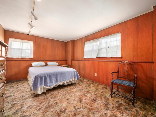 bedroom featuring wooden walls, rail lighting, and carpet floors