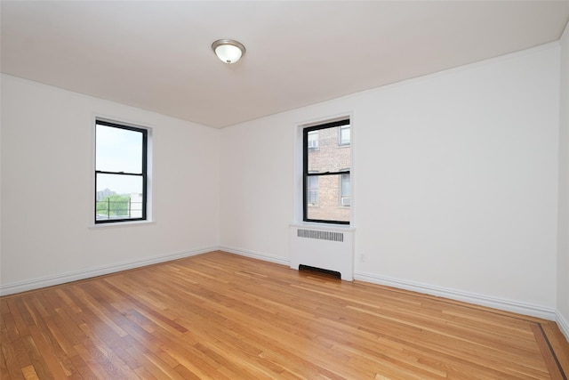 spare room with light wood-style floors, baseboards, and radiator heating unit