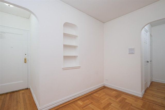 interior space with arched walkways, baseboards, crown molding, and built in shelves