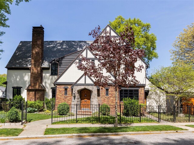 tudor house featuring a fenced front yard, stucco siding, and a chimney