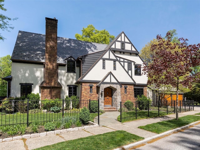 tudor home with a high end roof, a fenced front yard, brick siding, stucco siding, and a chimney