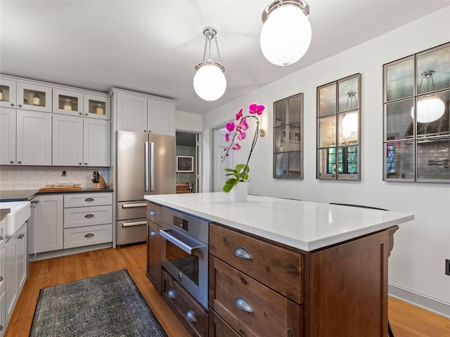 kitchen featuring glass insert cabinets, light wood-style flooring, decorative backsplash, and stainless steel appliances