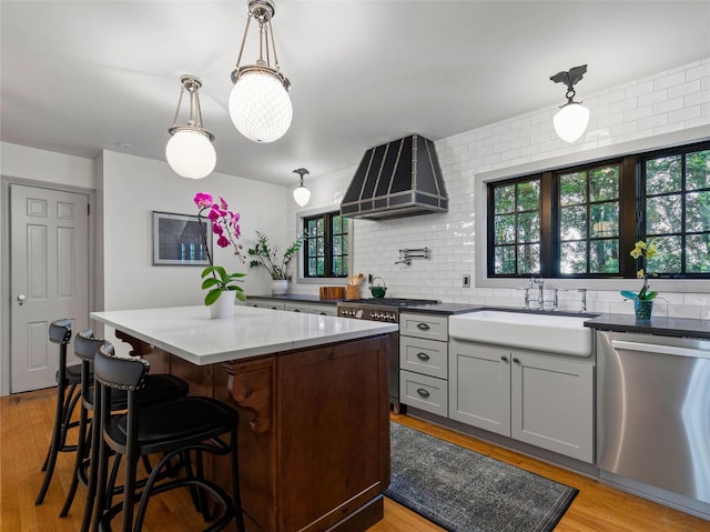 kitchen featuring wall chimney range hood, a center island, a sink, light wood-style flooring, and appliances with stainless steel finishes