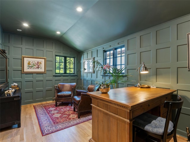 office area featuring light wood finished floors, lofted ceiling, and a decorative wall