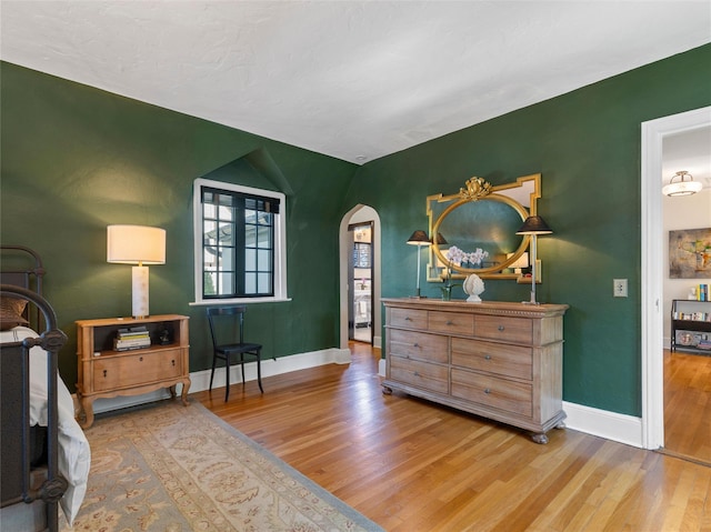 bedroom with arched walkways, baseboards, and wood finished floors