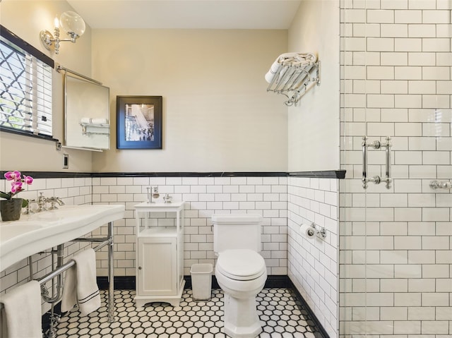full bathroom featuring toilet, tile walls, tiled shower, a wainscoted wall, and a sink
