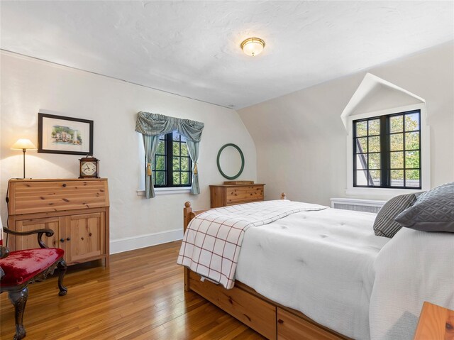 bedroom with baseboards, light wood-style flooring, and lofted ceiling