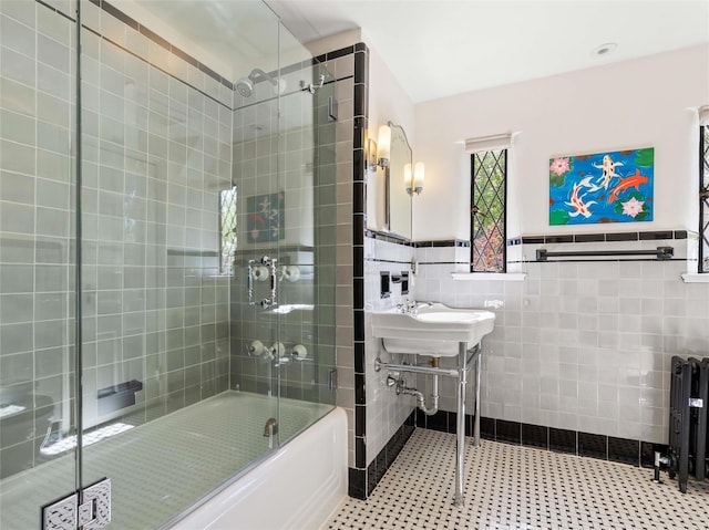 full bathroom featuring a sink, radiator heating unit, a wainscoted wall, tile walls, and combined bath / shower with glass door