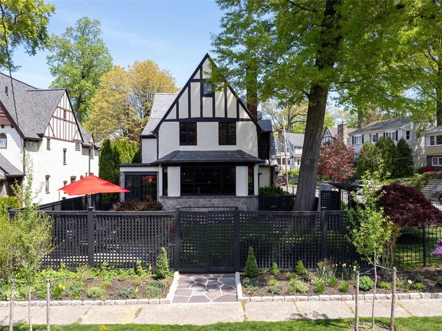 tudor house featuring a fenced front yard, a gate, stone siding, and stucco siding