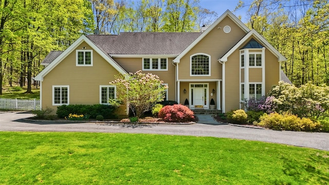 traditional-style home featuring fence, a shingled roof, and a front lawn
