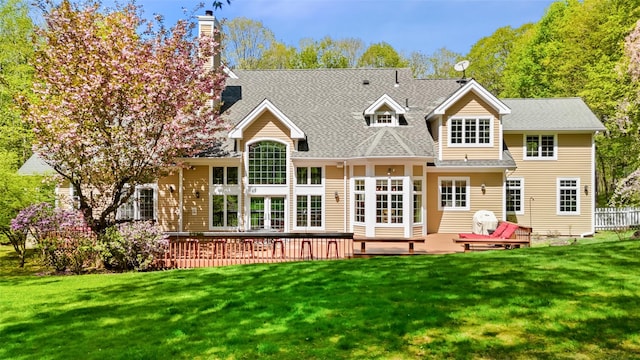 rear view of house with a wooden deck, a shingled roof, a yard, and a chimney