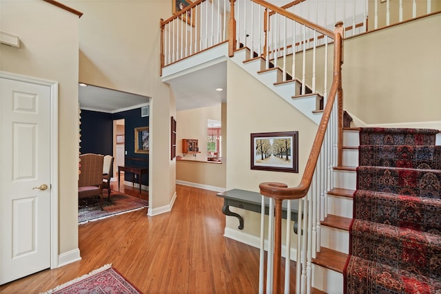 stairway featuring baseboards, wood finished floors, and a high ceiling
