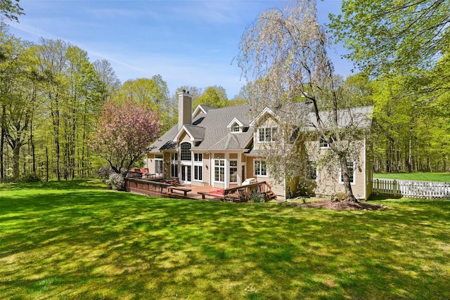 rear view of property featuring fence, a wooden deck, a chimney, and a yard